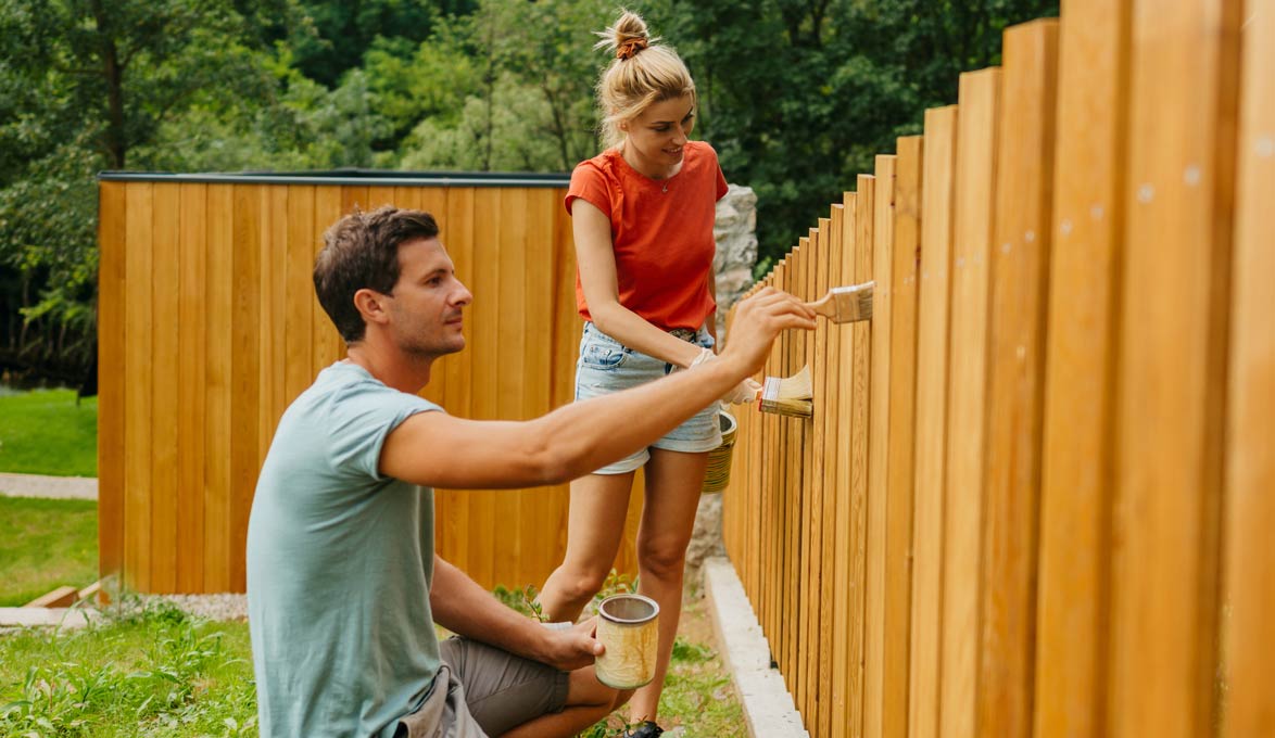 A couple staining a fence in their backyard