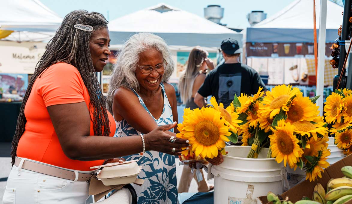 Two women look at a small business booth at a local market